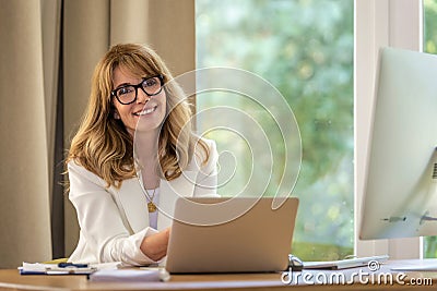 Confident mid aged business woman sitting at desk and using laptop for work Stock Photo