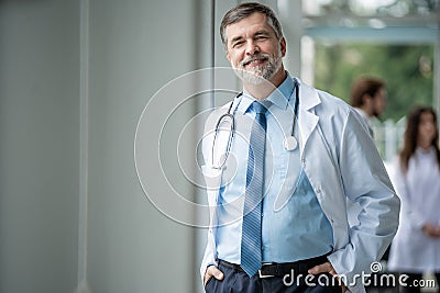 Confident smiling doctor posing in the hospital with medical team working on the background. Stock Photo