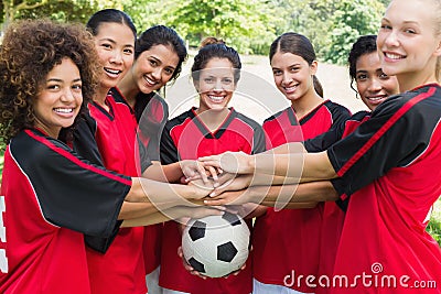 Confident soccer team stacking hands on ball Stock Photo