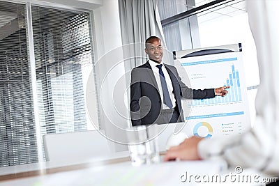 Confident young businessman pointing towards graph while giving presentation in office Stock Photo