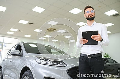 Confident young caucasian businessman shop assistant standing in car automobile dealer shop Stock Photo