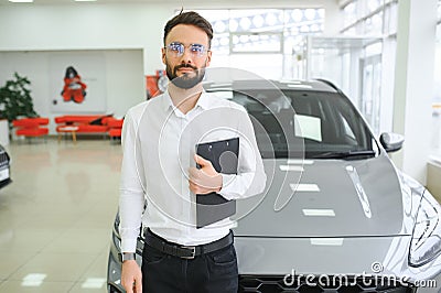 Confident young caucasian businessman shop assistant standing in car automobile dealer shop Stock Photo