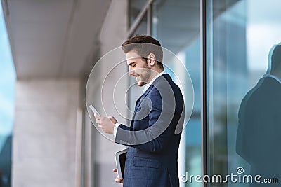 Confident young enterpreneur using his cellphone for online communication near business center Stock Photo