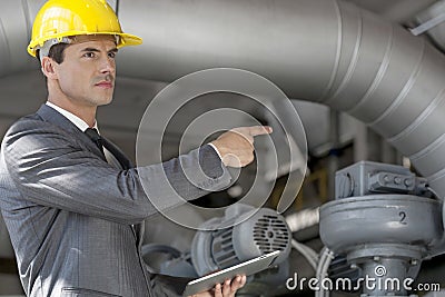 Confident young male manager with digital tablet pointing at machinery in industry Stock Photo