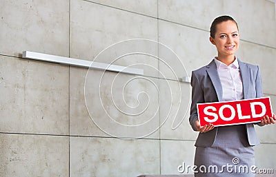 Portrait of confident young saleswoman holding sold placard while standing against wall in apartment Stock Photo