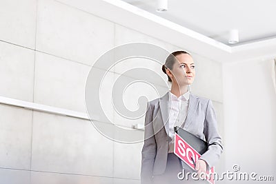 Confident young saleswoman looking away while standing with sold placard and document against wall in apartment Stock Photo