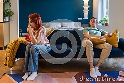 Conflict, quarrel. Haughty husband sit on couch feels annoyed, offended. Man tyrant humiliates wife Stock Photo