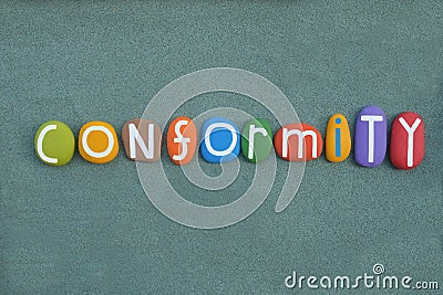 Conformity, creative word composed with multi colored stone letters over green sand Stock Photo