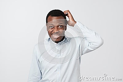 Confused african man scratching head while looking at camera and standing over gray background. Stock Photo