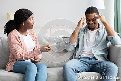 Confused black lady showing her stressed boyfriend pregnancy test Stock Photo