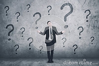 Confused caucasian businessman with question marks on the wall Stock Photo