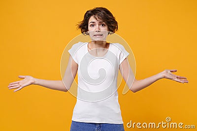 Confused perplexed young brunette woman in white t-shirt posing isolated on yellow orange background studio portrait Stock Photo