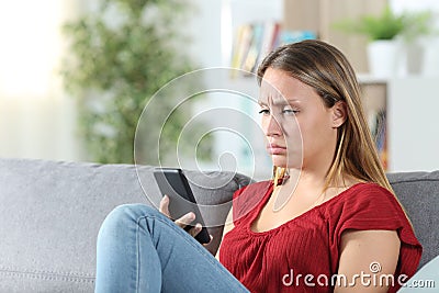 Confused woman after looking at her phone in the couch Stock Photo