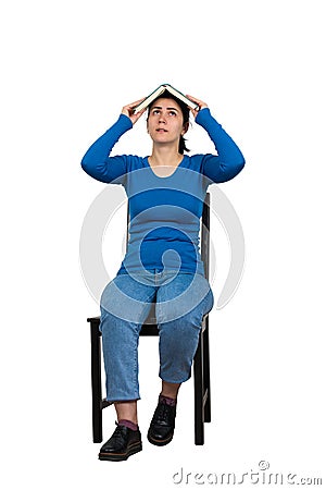 Confused woman student, seated on a chair, keeps open book over head isolated on white. Difficult task concept, discontent girl Stock Photo