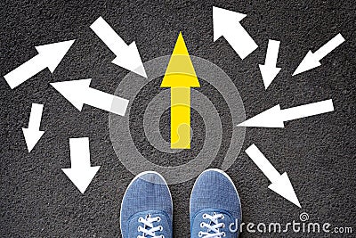 Confusing direction arrows on asphalt ground, feet and shoes on floor, personal orientation concept Stock Photo