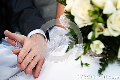 Connected hands of happy newlyweds without ring with bridal bouquet Stock Photo