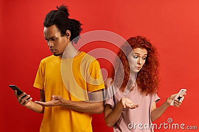 Connection error. Black millennial man and redhead woman looking at smartphones, annoyed with discharged or broken Stock Photo