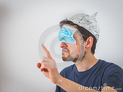 Conspiracy theory concept: Young angry man wearing aluminum hat and face mask over the eyes is gesturing angry Stock Photo