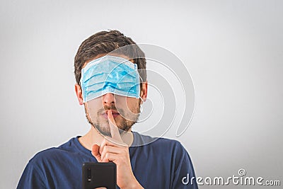 Conspiracy theory concept: Young man with face mask over the eyes is making a psst! gesture Stock Photo