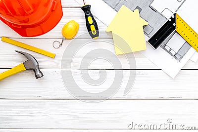 Construction concept. Helmet, tools on work desk, house cutout on white wooden background top-down frame copy space Stock Photo