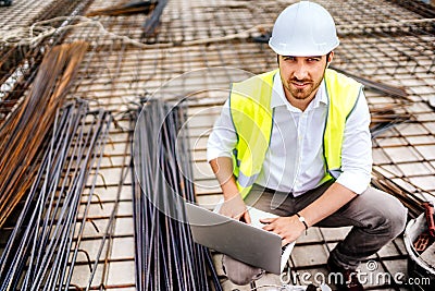 construction engineer working on laptop, wearing safety equipement and coordinating workers Stock Photo