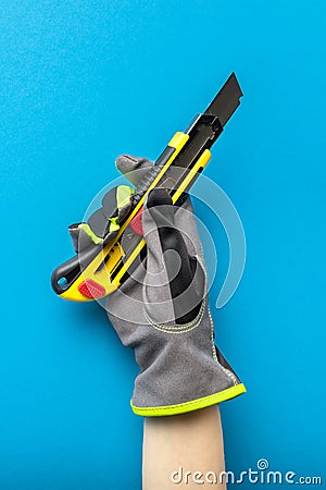 Construction knife. Stationery knife in hand with a glove on a blue background. Construction and renovation theme. Place for text Stock Photo