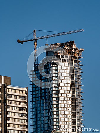 A crane is seen at the top of a high rise building under construction Stock Photo