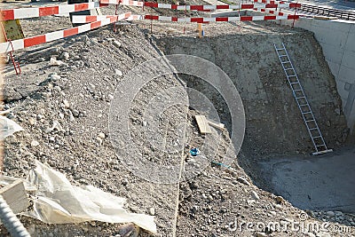 Construction pit or shaft with a metal ladder for better access surrounded by barrier planks in red and white Stock Photo