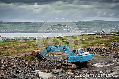 Construction site in a field with blue color excavator working. Dark dramatic sky, Stock Photo