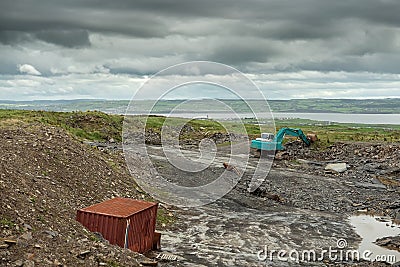 Construction site in a field with blue color excavator working. Dark dramatic sky, West of Ireland Stock Photo