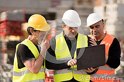 Construction site manager and two workers using pc laptop Stock Photo