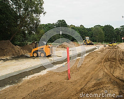 Construction site of new road in suburban. Yellow excavator, road roller and skid loader. Green trees. Stock Photo