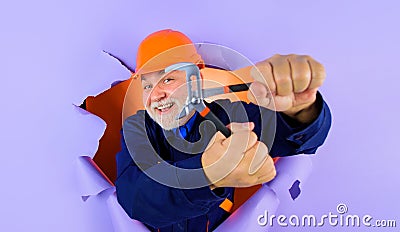 Construction worker or builder in hard hat with adjustable wrench looking through paper hole. Bearded man in uniform Stock Photo