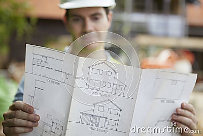 Construction Worker On Building Site Looking At House Plans Stock Photo