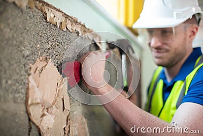 Construction Worker With Chisel Removing Plaster From Wall In Renovated House Stock Photo