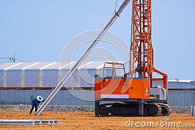 Construction worker with crawler pile driver machine lifting concrete piling for install industrial building structure Stock Photo