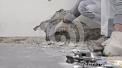 Construction worker hands with gloves working with spatula scrape off the plaster from the wall for house renovation, close up Stock Photo