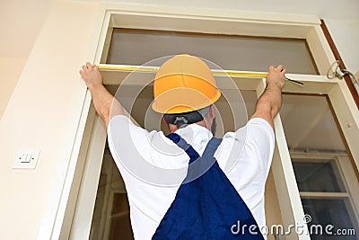 Construction worker and handyman is working on renovation of apartment. Builder is measuring of room door using measure tape. Stock Photo