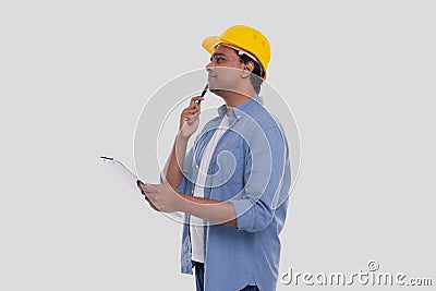 Construction Worker Holding Clipboard in Hands Watching up. Man Thinking. Architect Holding Blueprints. Yellow Hard Helmet Stock Photo