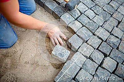 Construction worker laying cobblestones and stone blocks on pavement Stock Photo