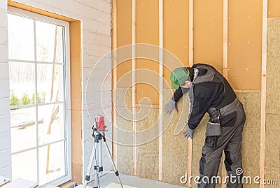 The worker makes finishing works of walls with a white wooden board, using laser line level. Building heat-insulating Stock Photo