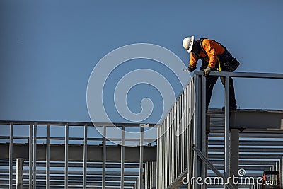 Construction worker on top of steel framing in white hard hat and orange long sleeve shirt Stock Photo