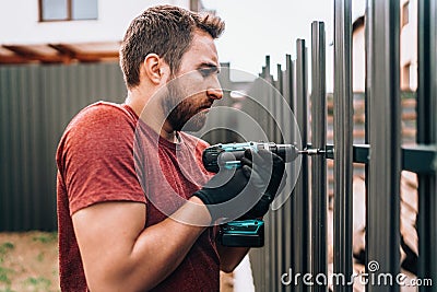 Construction worker using electrical screwdriver and mounting metal elements on fence Stock Photo