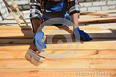 Construction worker is working with wooden beam. The worker brushes the preservative liquid on the folded boards and boards. Stock Photo