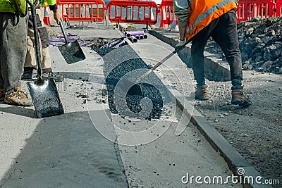 Construction workers placing hot tarmac after installation of new underground services, kerbs Stock Photo