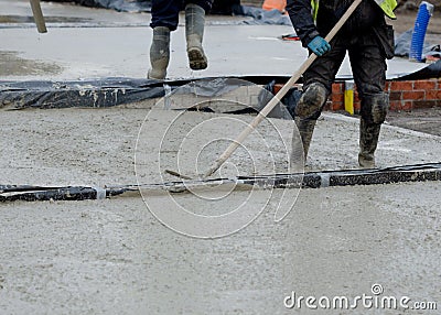 Construction workers pouring wet self levelling concrete screed during ground floor construction of new residential house and Stock Photo