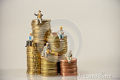 Construction workers sitting on money coin piles. Stock Photo