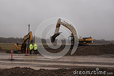 Construction workers stand by while they watch two Caterpillar excavators dig utility line for new freeway overpass on ramp. Editorial Stock Photo