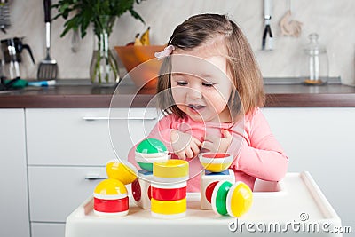 Construction a 2 year old girl with long hair plays with a designer at home, builds towers, rejoices at successes. Stock Photo