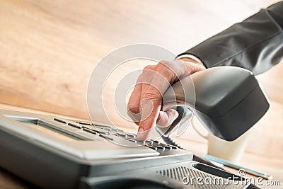 Consultant holding the receiver of a desk phone while dialing Stock Photo